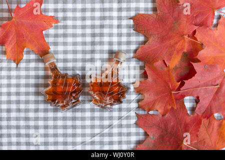 Ahornsirup in einer Flasche in einer Form der Maple Leaf. Red maple leaf Hintergrund. Stockfoto
