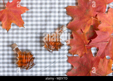 Ahornsirup in einer Flasche in einer Form der Maple Leaf. Red maple leaf Hintergrund. Stockfoto