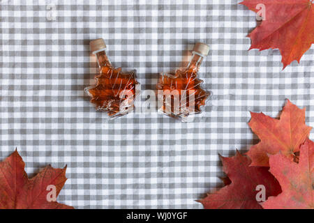 Ahornsirup in einer Flasche in einer Form der Maple Leaf. Red maple leaf Hintergrund. Stockfoto