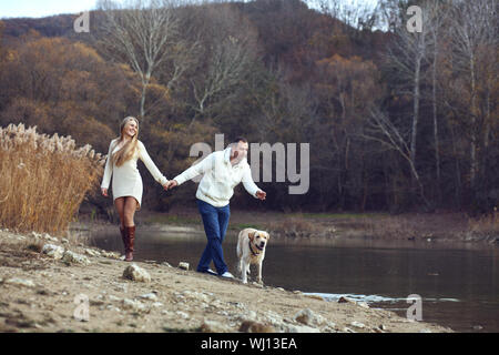 Junge glückliches Paar Wandern mit Hund in der Nähe der See im Herbst Stockfoto