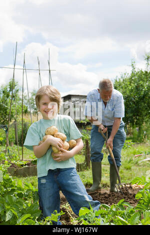 Portrait von Happy Boy holding Kartoffeln mit Großvater in der Gemeinschaft garten arbeiten