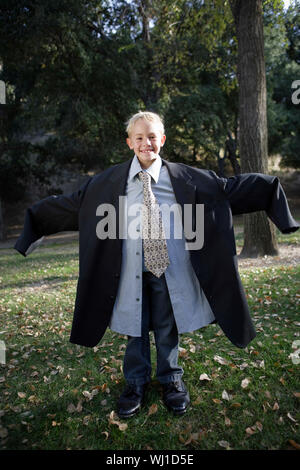 In voller Länge Porträt eines lächelnden Jungen tragen Übergröße Anzug im Freien Stockfoto