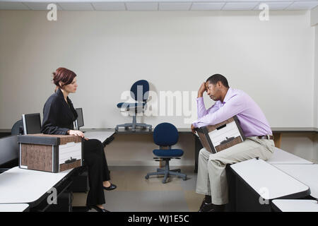 Volle Länge seitliche Sicht auf ein depressiver Mensch mit Kasten und weibliche Manager sitzen auf Schreibtisch Stockfoto