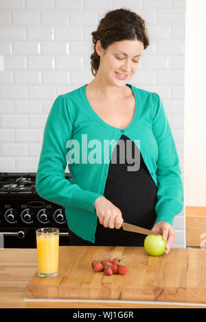 Schwangere junge Frau vorbereiten schneiden Obst in der Küche zu Hause. Stockfoto