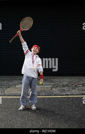 Volle Länge von einem Aufgeregten jungen männlichen Sieger heben Tennisschläger Stockfoto