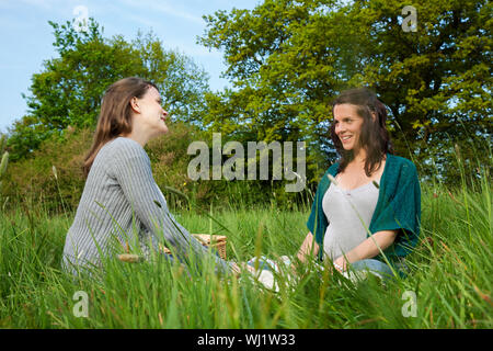 Zwei junge Frauen sitzen auf Grass gegen Bäume Stockfoto
