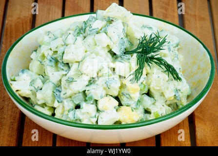 Köstliche Frisch zubereitete Cremige Kartoffel Salat garniert mit Dill in Beige Schüssel closeup auf Holzbrett Hintergrund Stockfoto