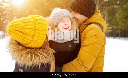 Portrait von Happy Family im Winter Tag. Mama und Papa sind Kuscheln küssen und ihren kleinen Sohn in Winter Park. Familie schöne Momente. Stockfoto