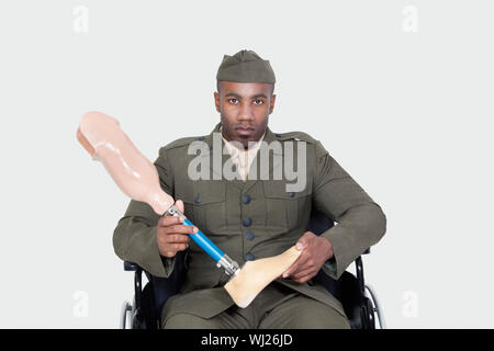 Portrait der junge Offizier im Rollstuhl holding Prothese Bein über grauer Hintergrund Stockfoto