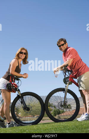 Volle Länge von einem kaukasischen Paar schiefen auf dem Fahrrad gegen den blauen Himmel Stockfoto