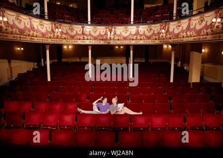 Volle Länge von zwei jungen Frauen im Theater sitzen mit Skripten Abschaltdruck Stockfoto