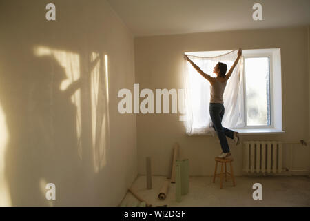 Volle Länge Rückansicht der jungen Frau fitting Vorhang in neue Wohnung Stockfoto