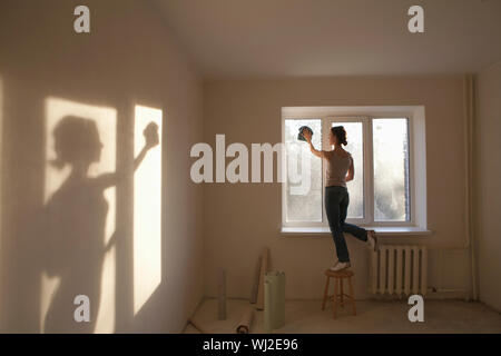 Volle Länge Rückansicht der jungen Frau, die Reinigung der Fenster in der neuen Wohnung Stockfoto
