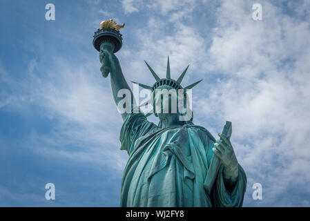 Schuss der Freiheitsstatue in New York City, USA. Der Schuß wird während ein schöner sonniger Tag mit blauem Himmel und weißen Wolken im Hintergrund