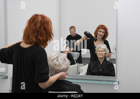 Gerne weibliche Stylist föhnen Haar der älteren Frau in Salon Stockfoto