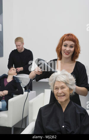 Gerne weibliche Stylist föhnen Haar der älteren Frau in Salon Stockfoto