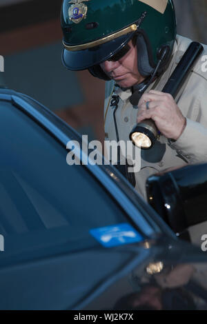 Im mittleren Alter Verkehrspolizist mit Taschenlampe untersucht, Auto Stockfoto