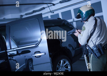 Ansicht der Rückseite des mittleren Alters traffic Cop, die Pistole am Auto in einer Garage. Stockfoto