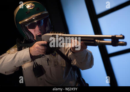 Zuversichtlich im mittleren Alter Polizist die Waffe gegen die Tür Stockfoto