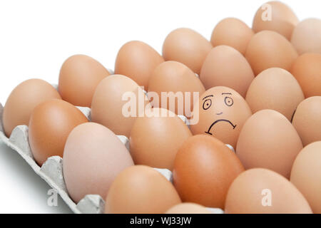Trauriges Gesicht auf ein Ei umgeben von einfachen braunen Eiern im Karton vor weißem Hintergrund gezeichnet Stockfoto