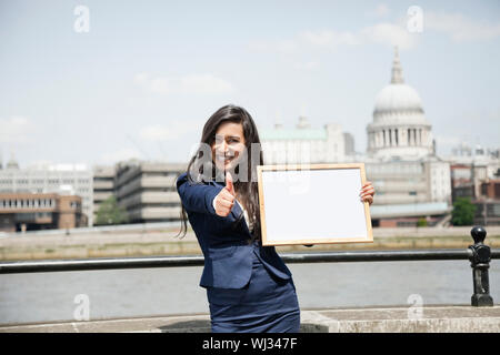 Indische Geschäftsfrau gestikulieren Daumen nach oben, wie sie Moodboard Schild mit St. Pauls Kathedrale im Hintergrund hält Stockfoto