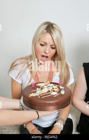Freunde, die überraschend junge Frau mit Geburtstagstorte Stockfoto