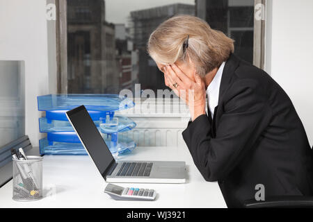 Seitenansicht der müde senior Geschäftsfrau vor Laptop am Schreibtisch im Büro Stockfoto