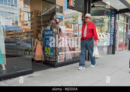 Ein Mann in einem roten T-Shirt Spaziergänge durch einen Sari shop auf 74th Street in den sehr unterschiedlichen Jackson Heights, Queens, New York City. Stockfoto