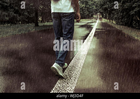 Ein Mann n Jeans und Sportschuhe allein n den Park Alley im Regen Stockfoto