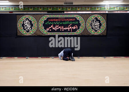 Ein gläubiger Muslim mann Bögen im Gebet vor der Koran Zitate an der Imam Al-Khoei Islamische Zentrum in Jamaica, Queens, New York City Stockfoto