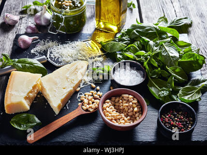 Frisches Basilikum, Parmesan, Pinienkerne, Knoblauch, Pfeffer, eine Flasche Olivenöl auf einem rustikalen Holztisch mit hausgemachtem Basilikumpesto sau Stockfoto