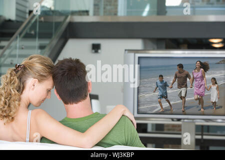 Rückansicht des jungen Paares vor dem Fernseher im Wohnzimmer Stockfoto