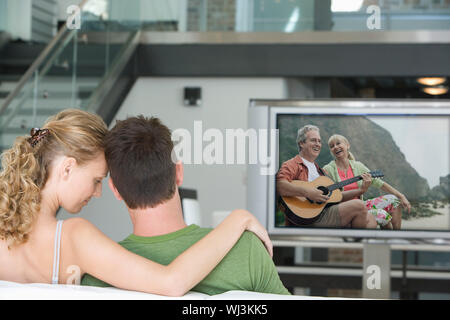 Rückansicht des jungen Paares vor dem Fernseher im Wohnzimmer Stockfoto