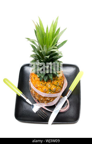 Ananas auf einem schwarzen Teller mit Klebeband Meter, Messer und Gabel isoliert auf weißem Hintergrund Stockfoto