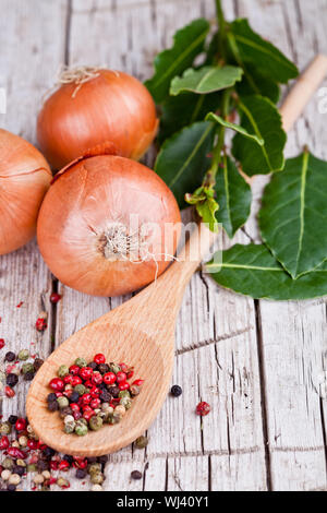 Frische Zwiebeln, Lorbeer und Pfefferkörner in einem Löffel auf rustikalen Holztisch Stockfoto