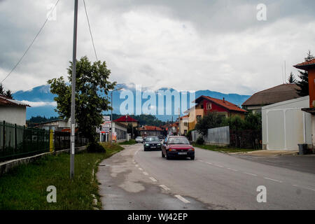 Zwei Autos fahren auf eine große Straße in Bulgarien mit einem malerischen Berg Hintergrund von Bäumen und Häusern umgeben Stockfoto