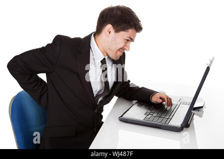 Geschäftsmann mit unteren Rücken Schmerzen vom sitzen mit einer schlechten Körperhaltung in seinem Bürostuhl auf seinem Laptop massieren den Rücken mit der Hand arbeiten Stockfoto