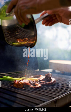 Koch gießen Sauce über Kalmar auf Octopus Stockfoto