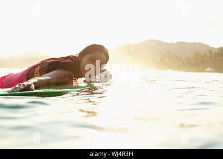 Portrait zuversichtlich, serene weibliche surfer Verlegung auf Surfboard im sonnigen Ozean Stockfoto