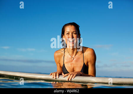 Portrait glückliche, selbstbewusste weibliche Surfer lehnte sich auf Surfbrett im Meer Stockfoto