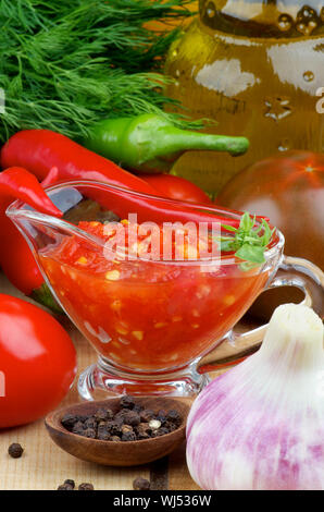 Anordnung der Bruschetta Sauce im Glas Soße Boot mit schwarzen Tomaten, Knoblauch, Chili Peppers und Glas Flasche Olivenöl closeup auf Holz- backgro Stockfoto