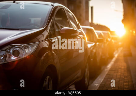Autos auf der Seite der Straße geparkt, mit Sonnenuntergang im Hintergrund. Stockfoto