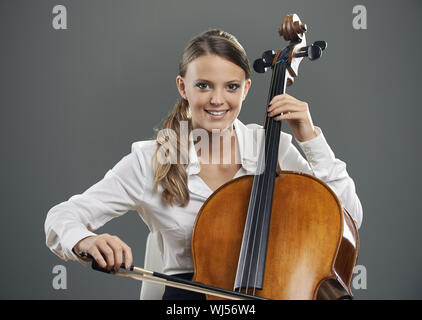 Lächelnde junge Frau Cellist auf grauem Hintergrund Stockfoto