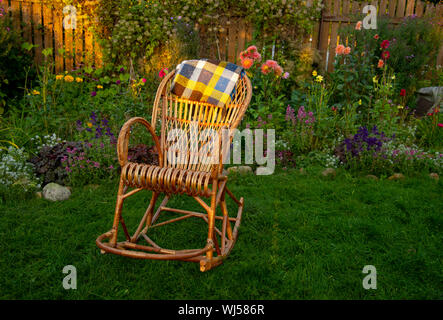 Ein rattan Schaukelstuhl sitzt auf einem Rasen in einem blühenden Garten Stockfoto