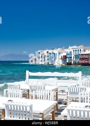 Weißen Tischen und Stühlen im Freien Restaurant am Ufer des Schwenkten blaue Meer an einem sonnigen Tag im Hafen der Insel Mykonos in Griechenland Stockfoto