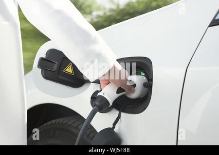 Weibliche Hand, die eine elektrische Stecker zum Aufladen von Elektroautos oder evt. Umweltfreundliche alternative Energiekonzept grüne Umgebung. Stockfoto