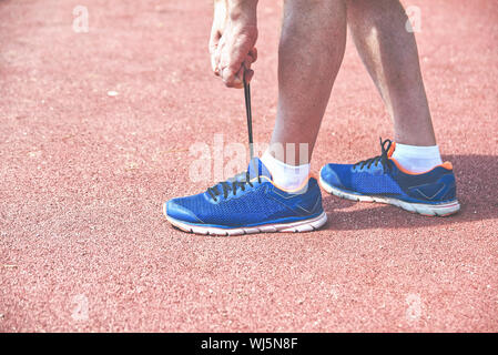 Jungen athletischen Mann Schnürung seine Turnschuhe bereit für sportliche Ausbildung und laufen auf einer roten Piste. Ausdauer und Gesundheit Aktivität Konzept mit Kopie Raum Stockfoto