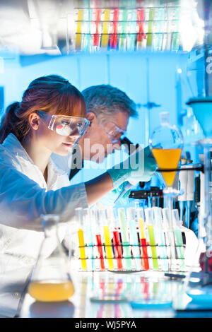 Attraktive junge Wissenschaftlerin und ihrem älteren männlichen Vorgesetzten Pipettieren und microscoping im Life Science Research Laboratory (Biochemie, Gen Stockfoto