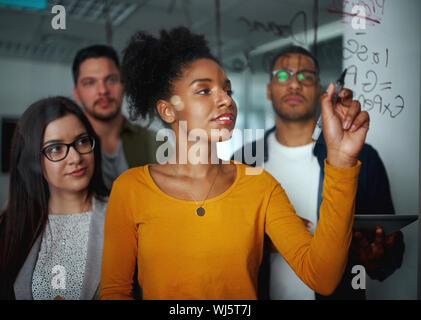 Portrait einer jungen Unternehmerin im modernen Büro stehen mit ihren Kolleginnen und Kollegen schreiben auf Glas mit schwarzem Marker Stockfoto