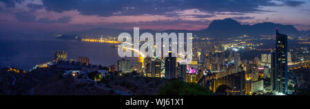 Die Lichter der Stadt von Benidorm nach Sonnenuntergang. Sky Purple und Silhouetten der Berge im Hintergrund. Stockfoto